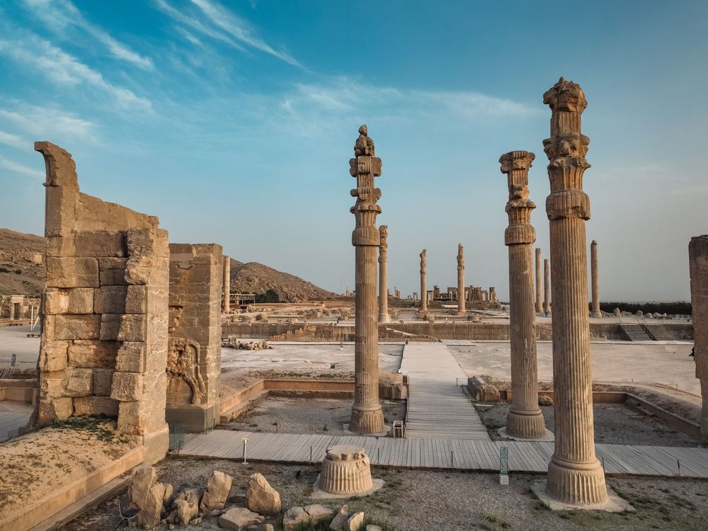 Ancient stone columns of Persepolis, Iran, a UNESCO World Heritage Site, with carved capitals rising above the ruins under a blue sky.