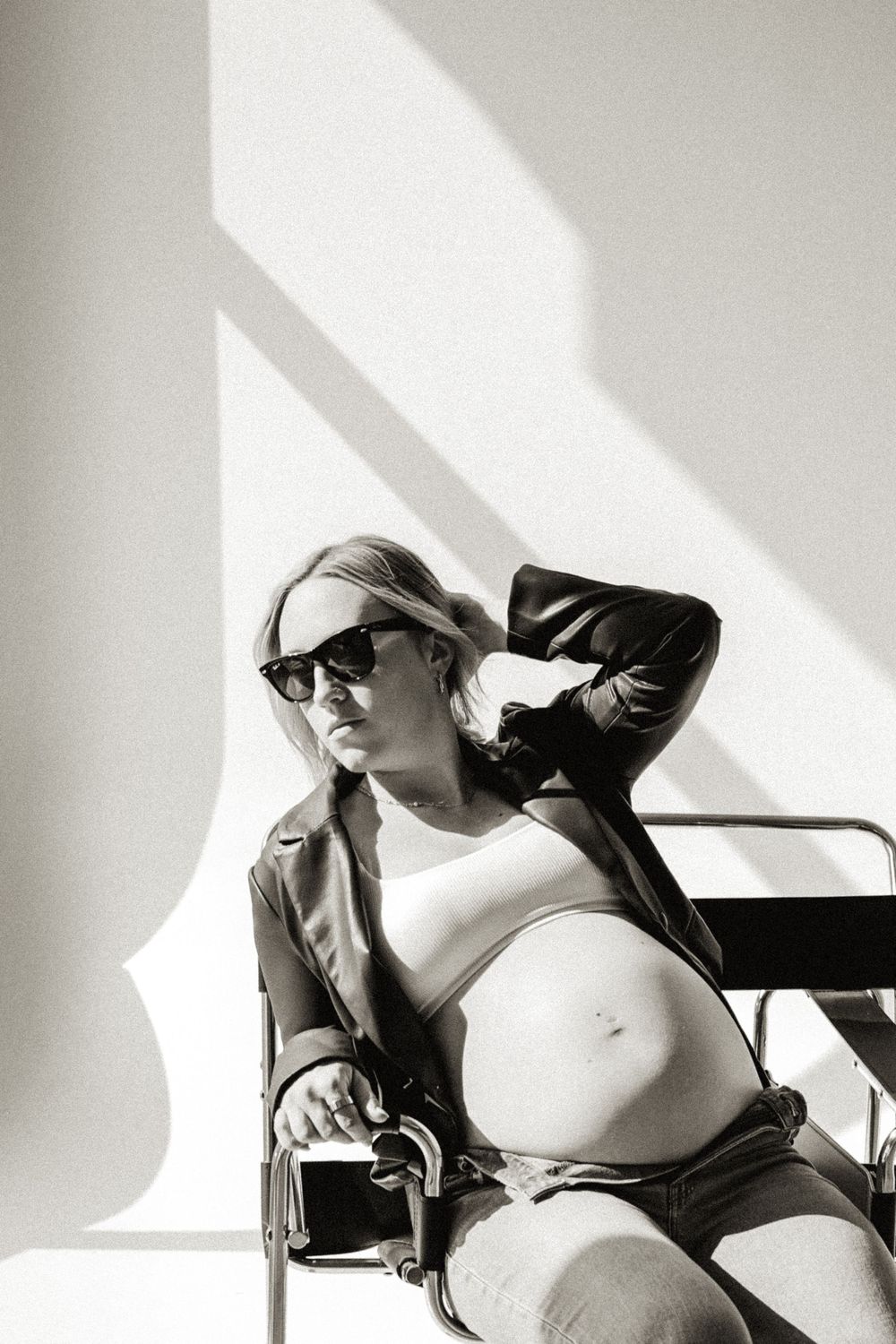 Effortless maternity portrait in black and white with a pregnant mother in jeans, sunglasses, and a leather jacket.