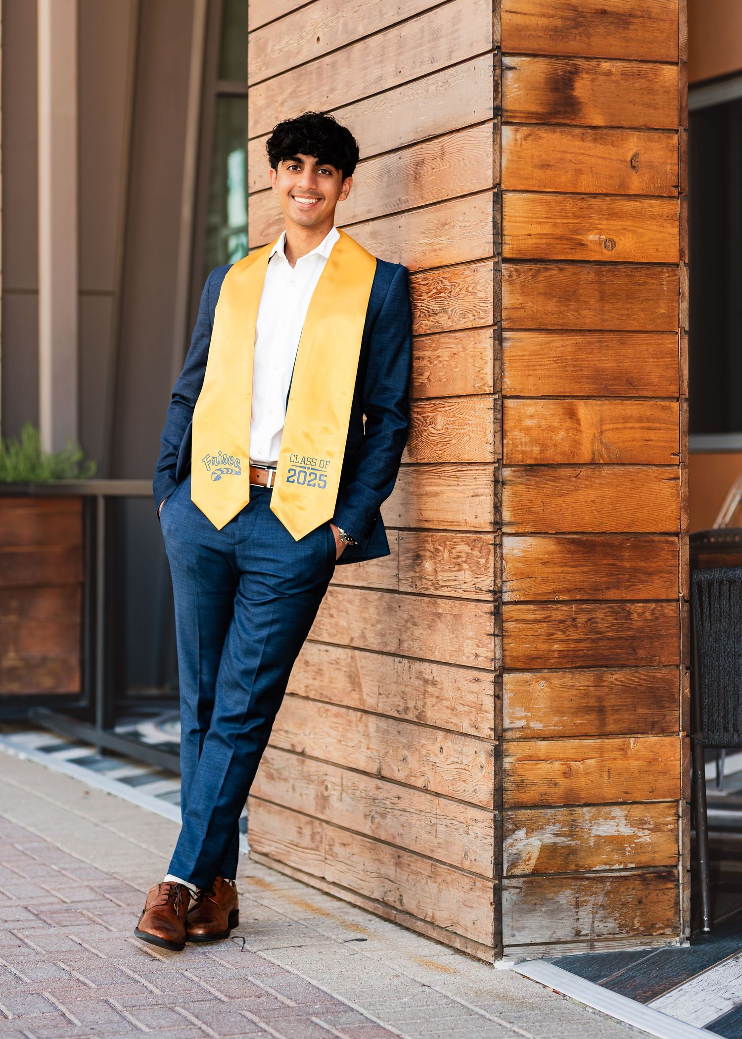 Young man in navy suit holding a soccer ball outdoors, smiling confidently in an urban setting.