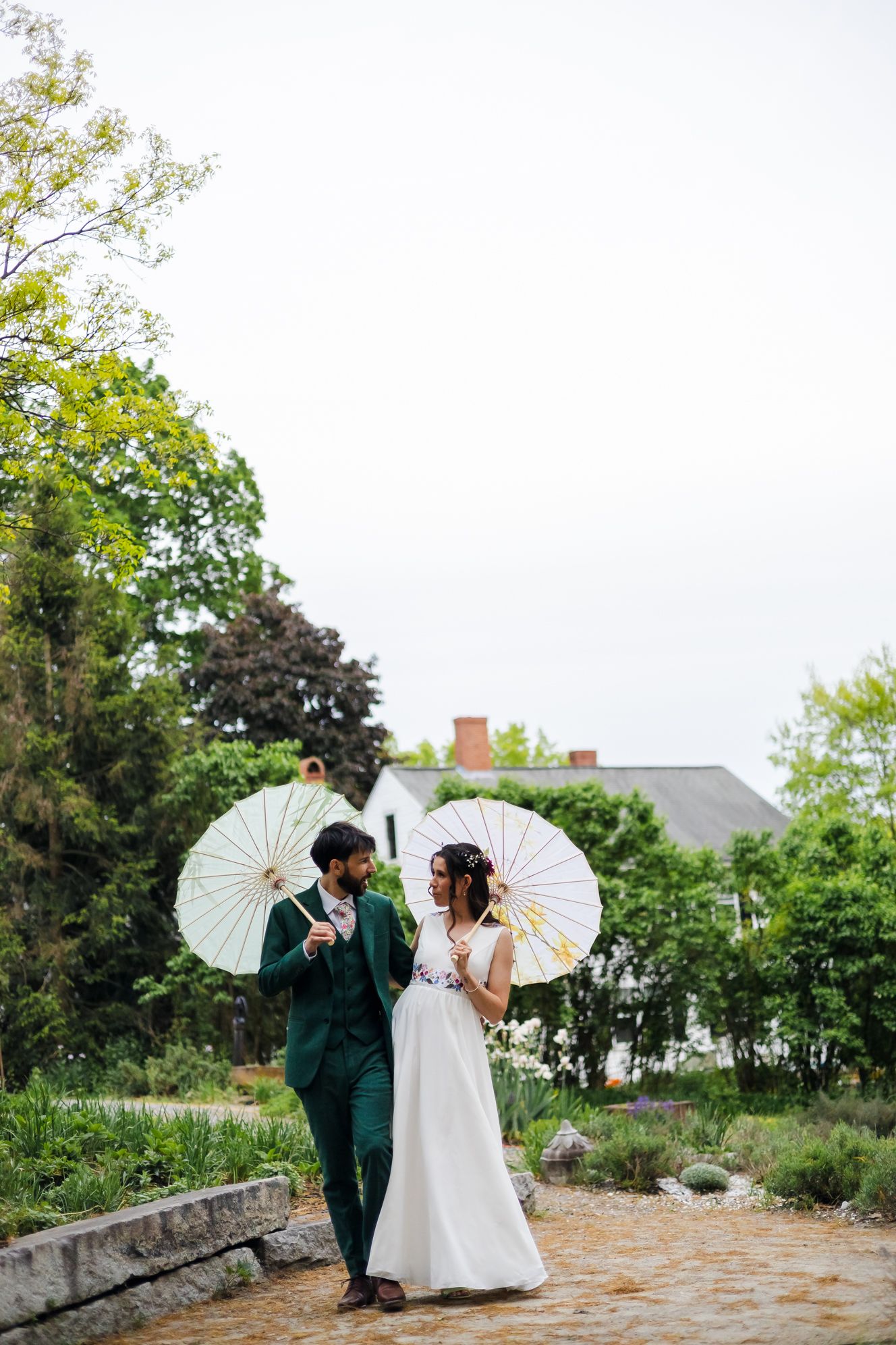 Bride and groom walking with white parasols in lush garden on their wedding day.