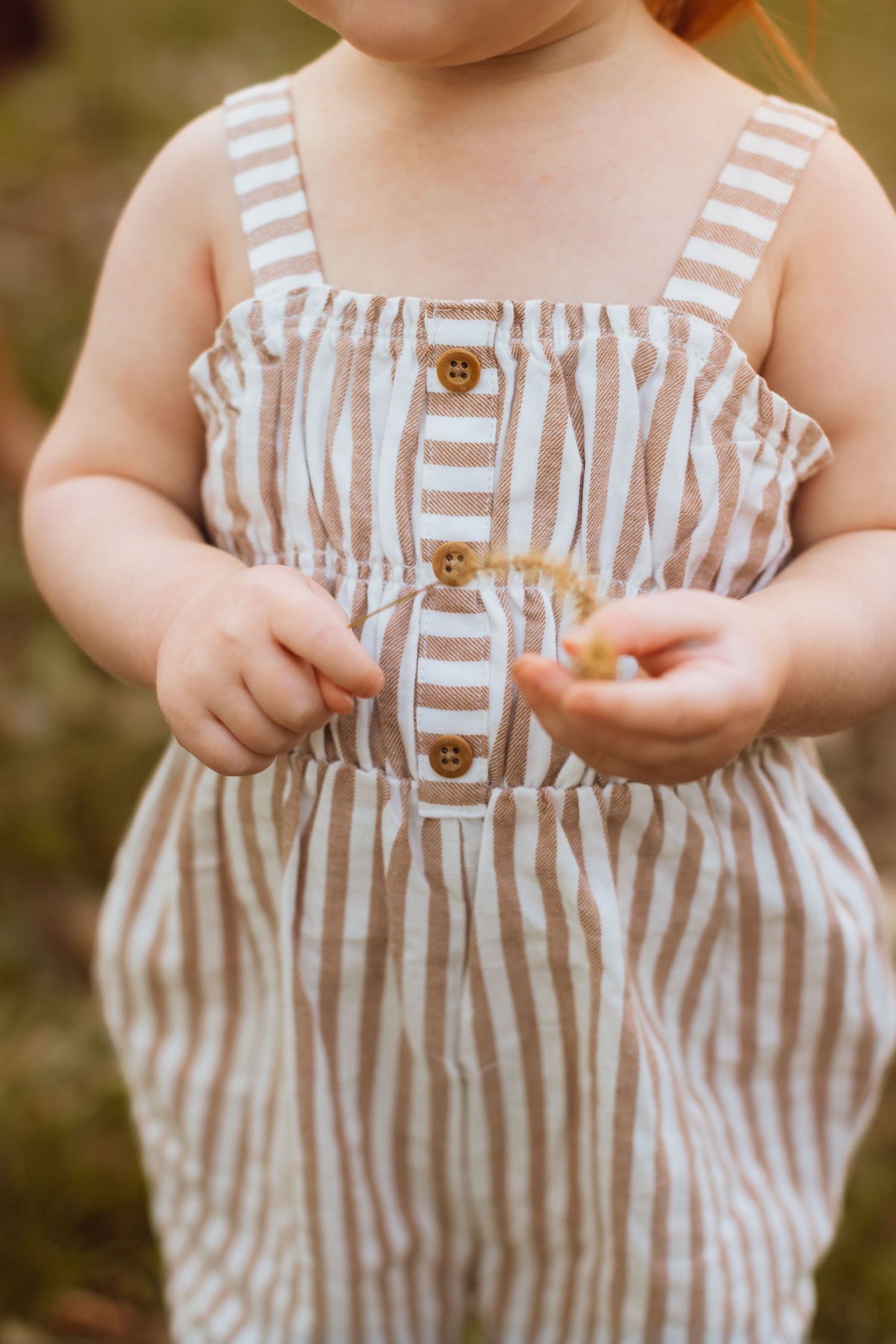 A close detail shot shows a toddler's chubby hands holding a piece of prairie grass during a Kansas City family photo session.
