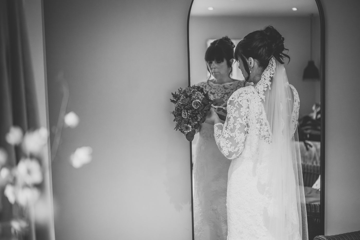 Bride in lace wedding dress holding bouquet, reflected in mirror, elegant black and white wedding photo.