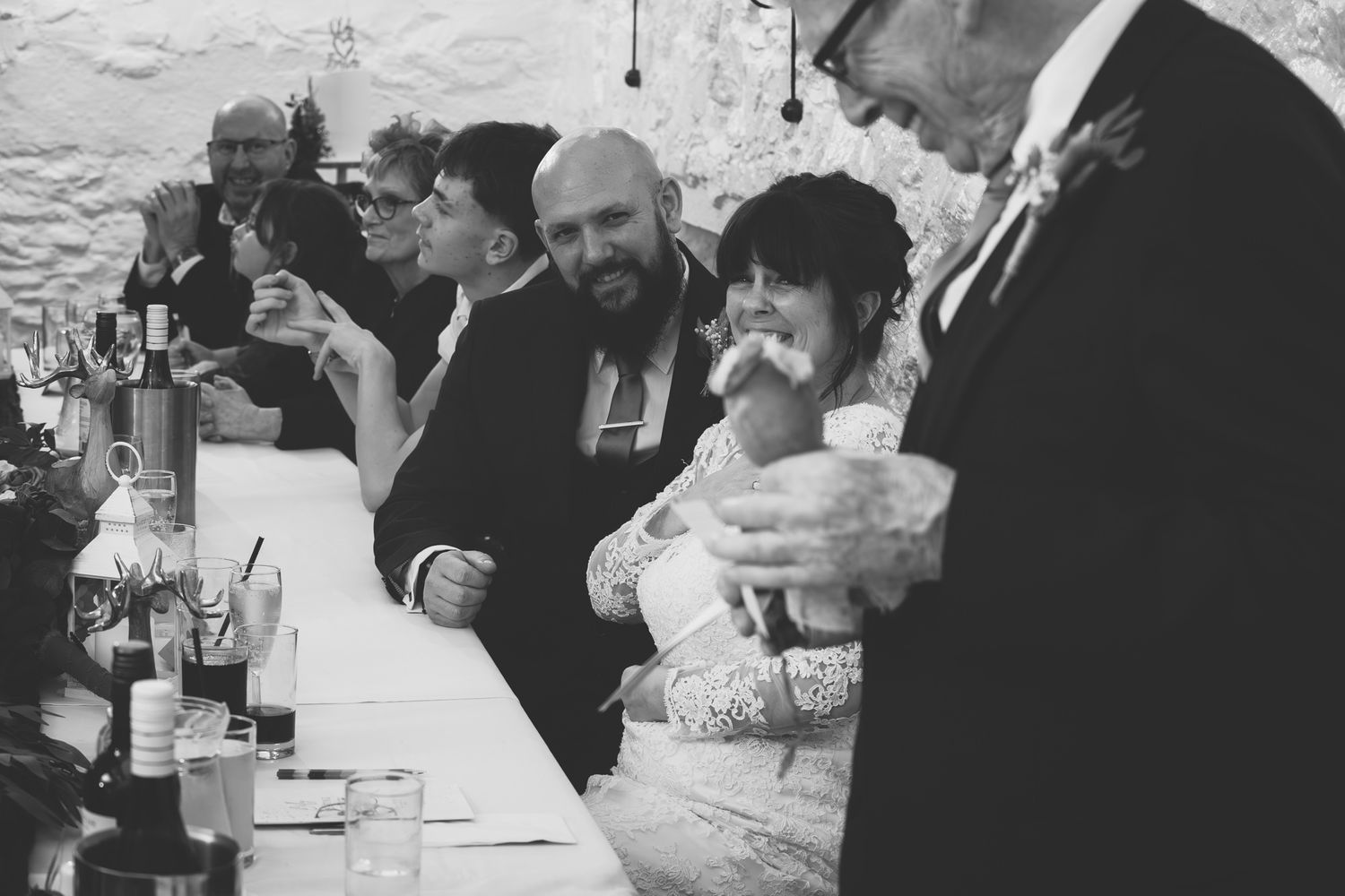 Black and white photo of bride and groom laughing with guests at wedding bar reception.