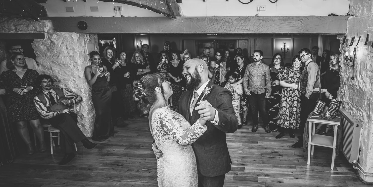 Bride and groom share their first dance surrounded by guests at a wedding reception in black and white.