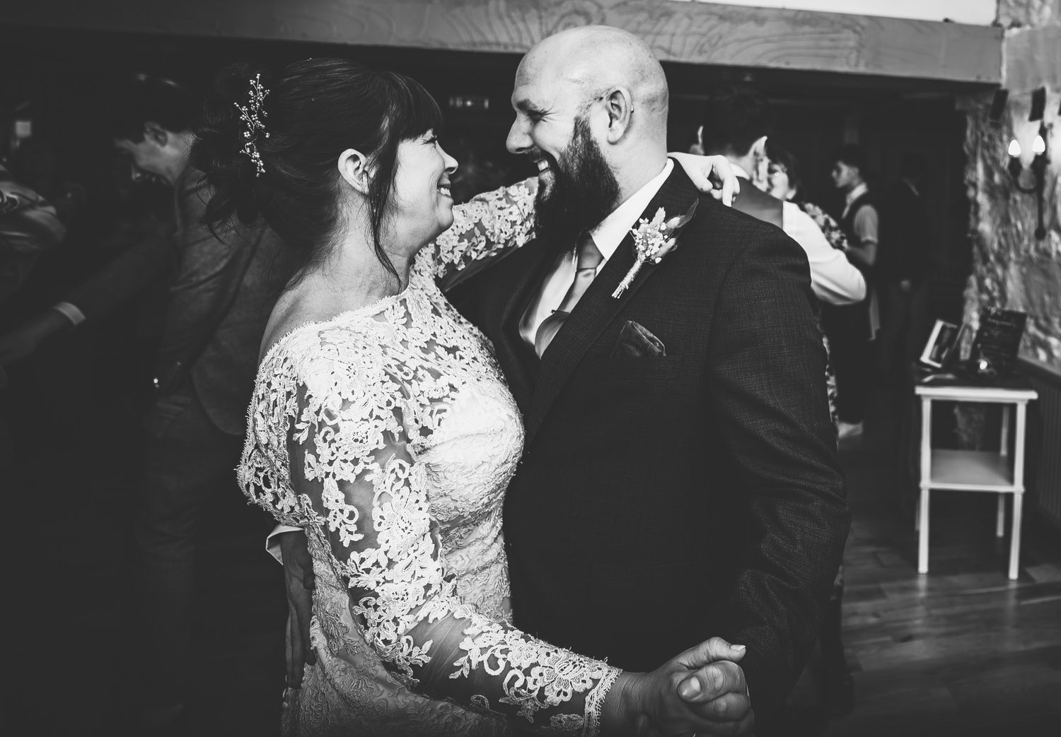 Bride in lace gown and bearded groom share an intimate first dance moment in black and white photo.