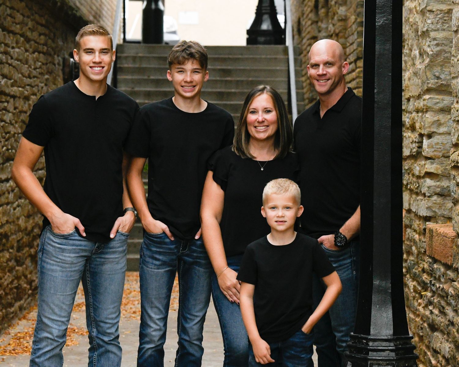 Family of five in matching black outfits posing on stone steps for a portrait photo.