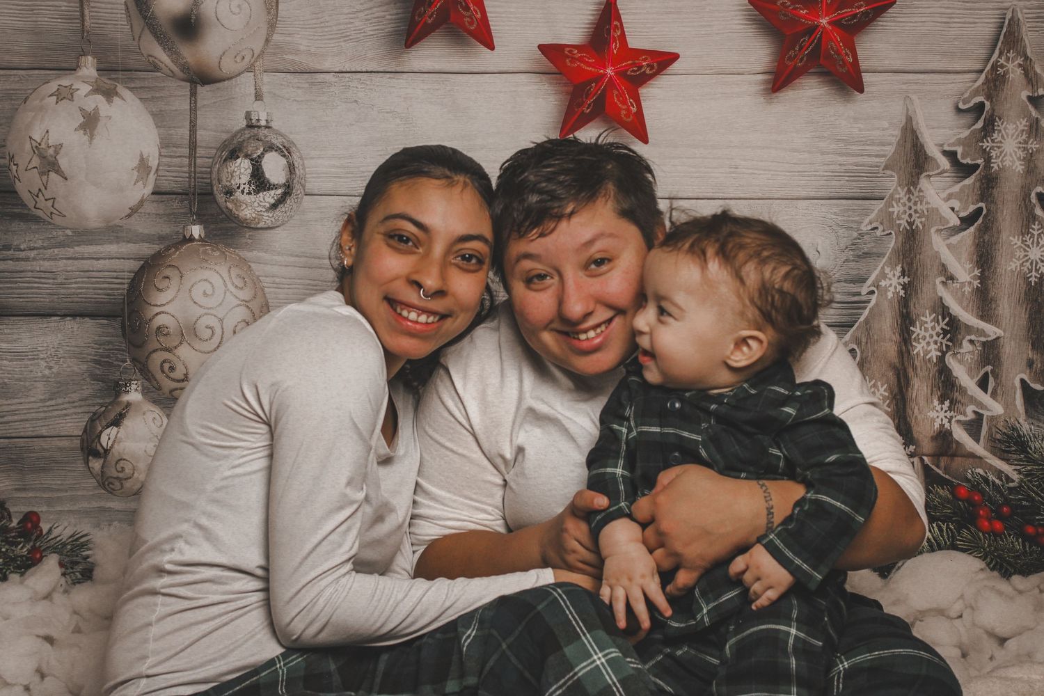 Family Christmas photo with two adults and a baby, festive star decorations and holiday backdrop.