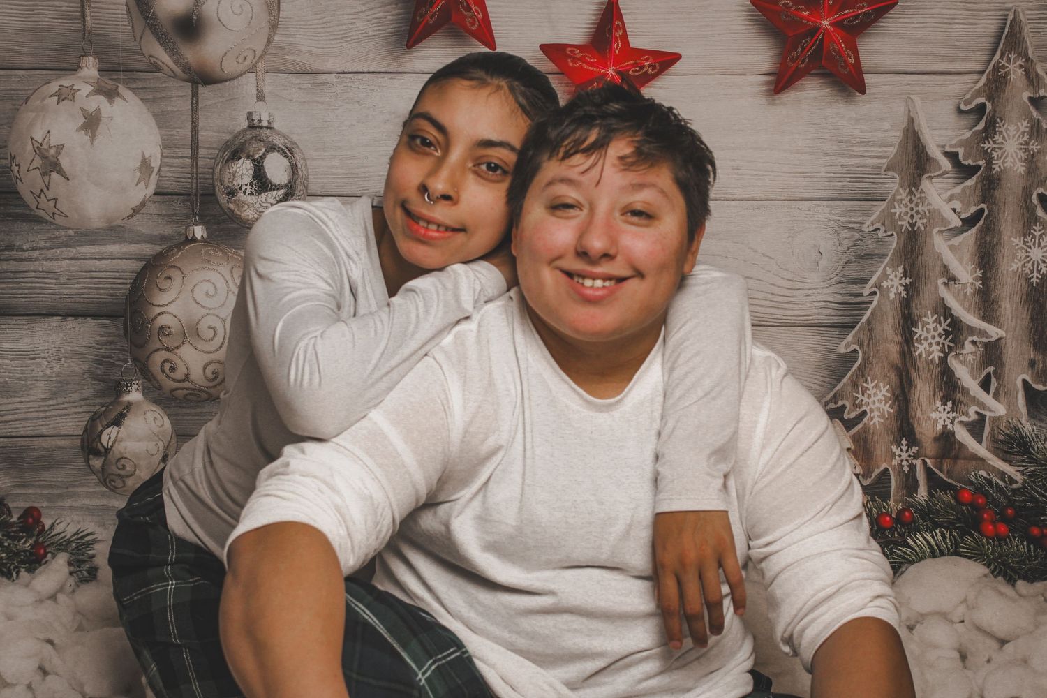 Two people in white shirts pose together in a festive Christmas photo with red stars and holiday decorations.