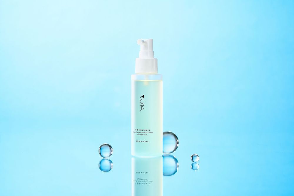 A clear spray bottle of facial mist on a reflective surface with water droplets against a blue background.