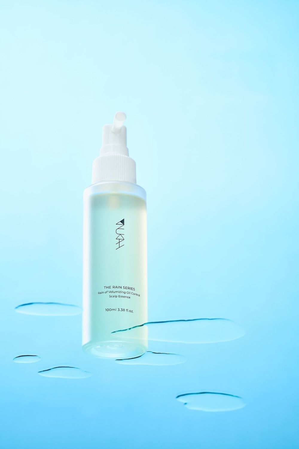 PUAH The Rain Serum hydrating facial essence in a clear pump bottle on a light blue background with water droplets.