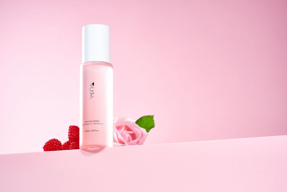 Pink skincare toner bottle with raspberries and rose on pastel pink background.