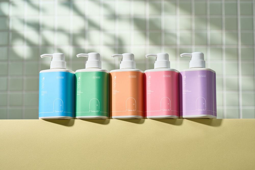 Five colorful pump dispenser bottles in blue, green, orange, pink, and purple arranged in a row on a yellow surface.