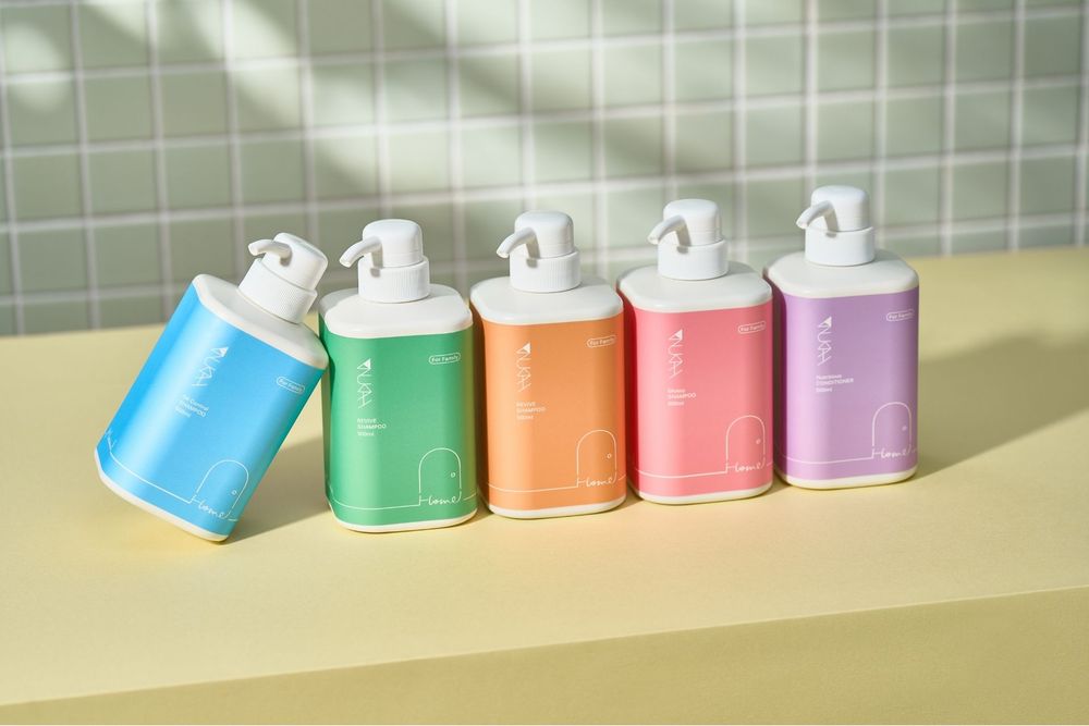 Five colorful pump bottles of skincare or soap products arranged on a yellow surface against a green tile background.