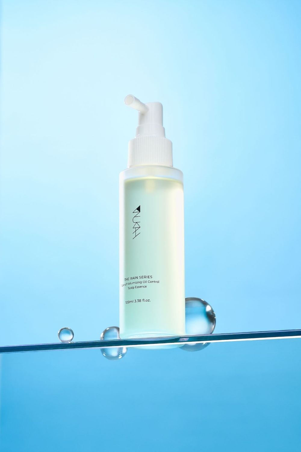 AURA skincare serum bottle with pump dispenser balanced on glass surface with water droplets on blue background.