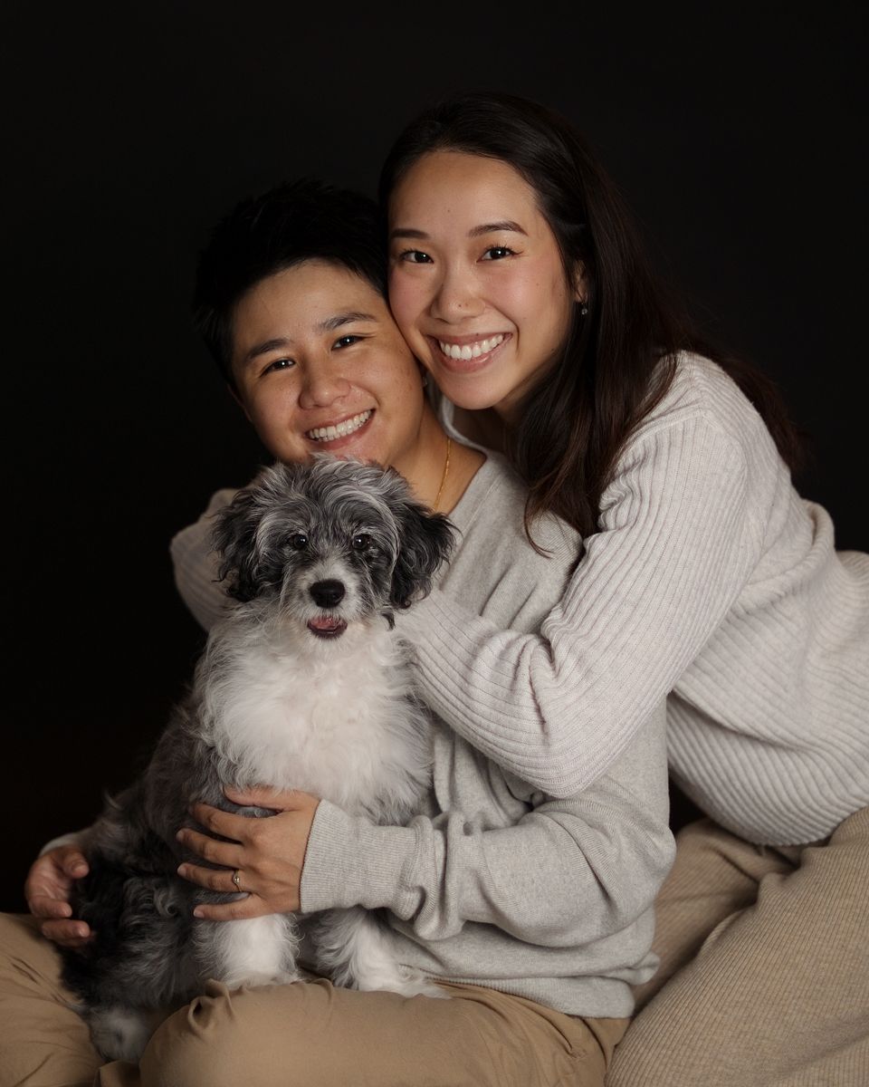 Two smiling people pose with a small fluffy black and white dog against a dark background in home photoshoot with in rouse hill