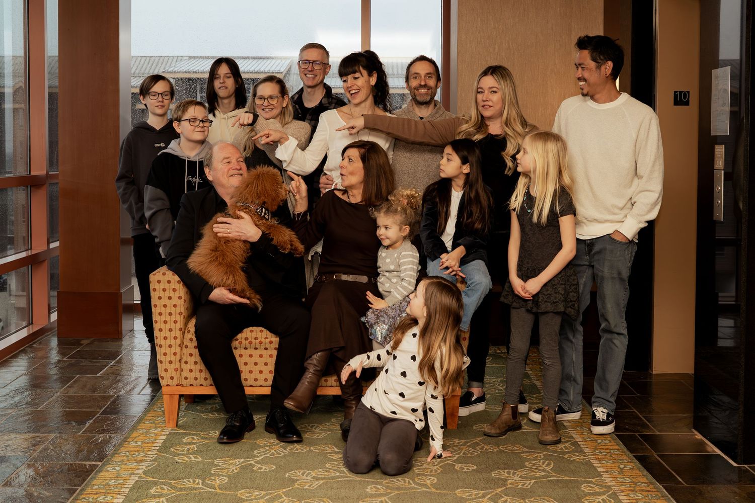 Large family group portrait posing together in a warmly lit lobby, smiling for a formal multi-generational family photo.