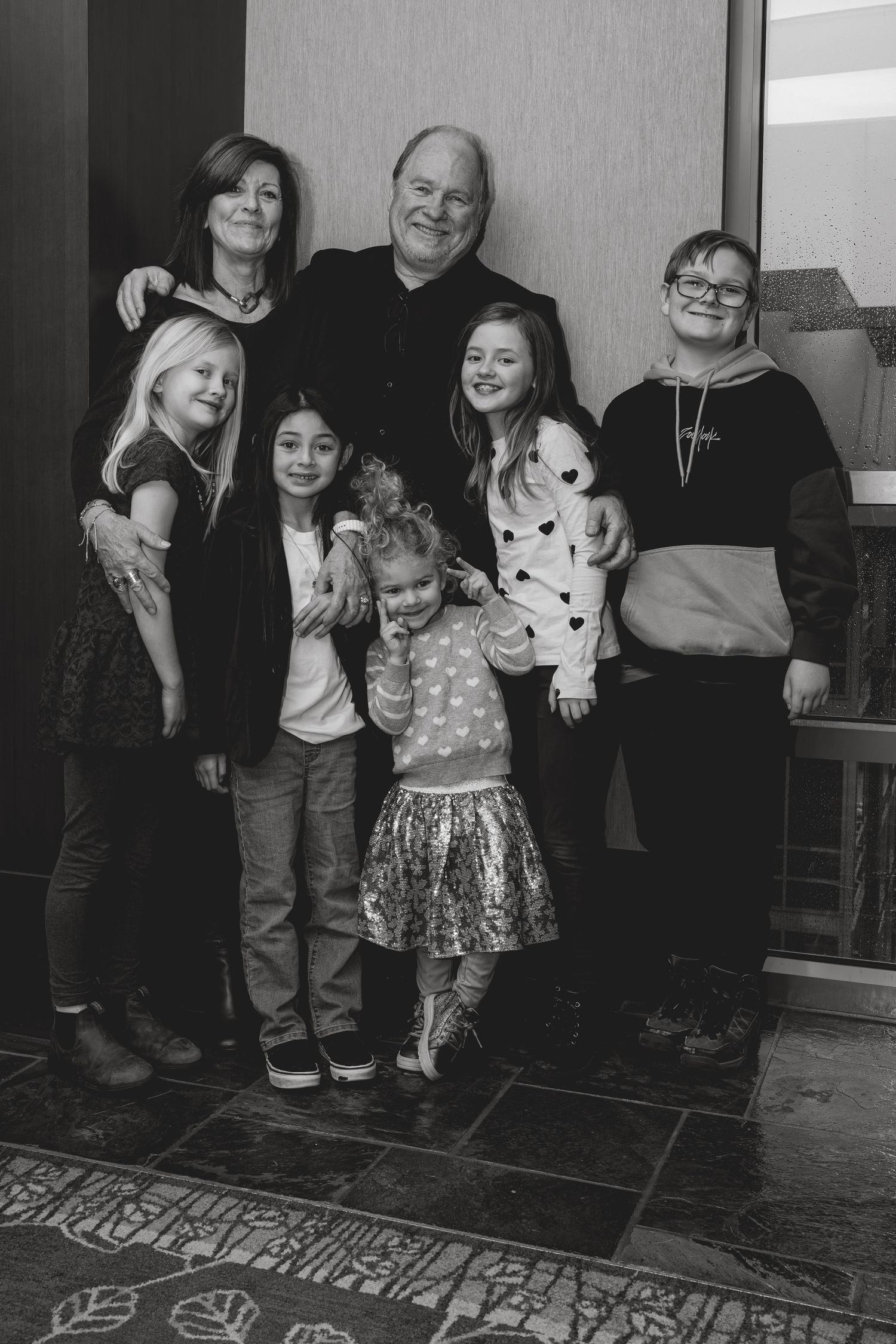 Black and white family portrait of grandparents posing with five young grandchildren indoors.