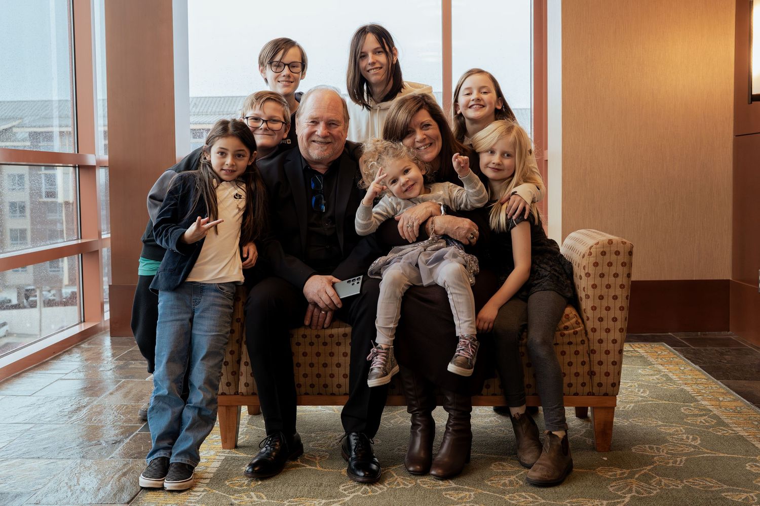 Family group portrait with elderly man seated among children and adults, smiling together in a modern indoor setting.