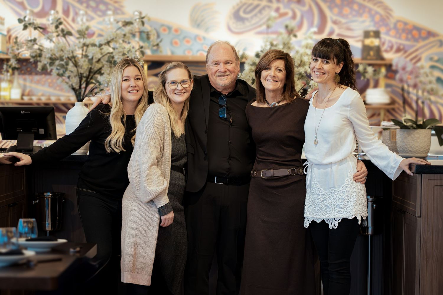 Five smiling people pose together in a warmly decorated restaurant, dressed in elegant attire for a special occasion.