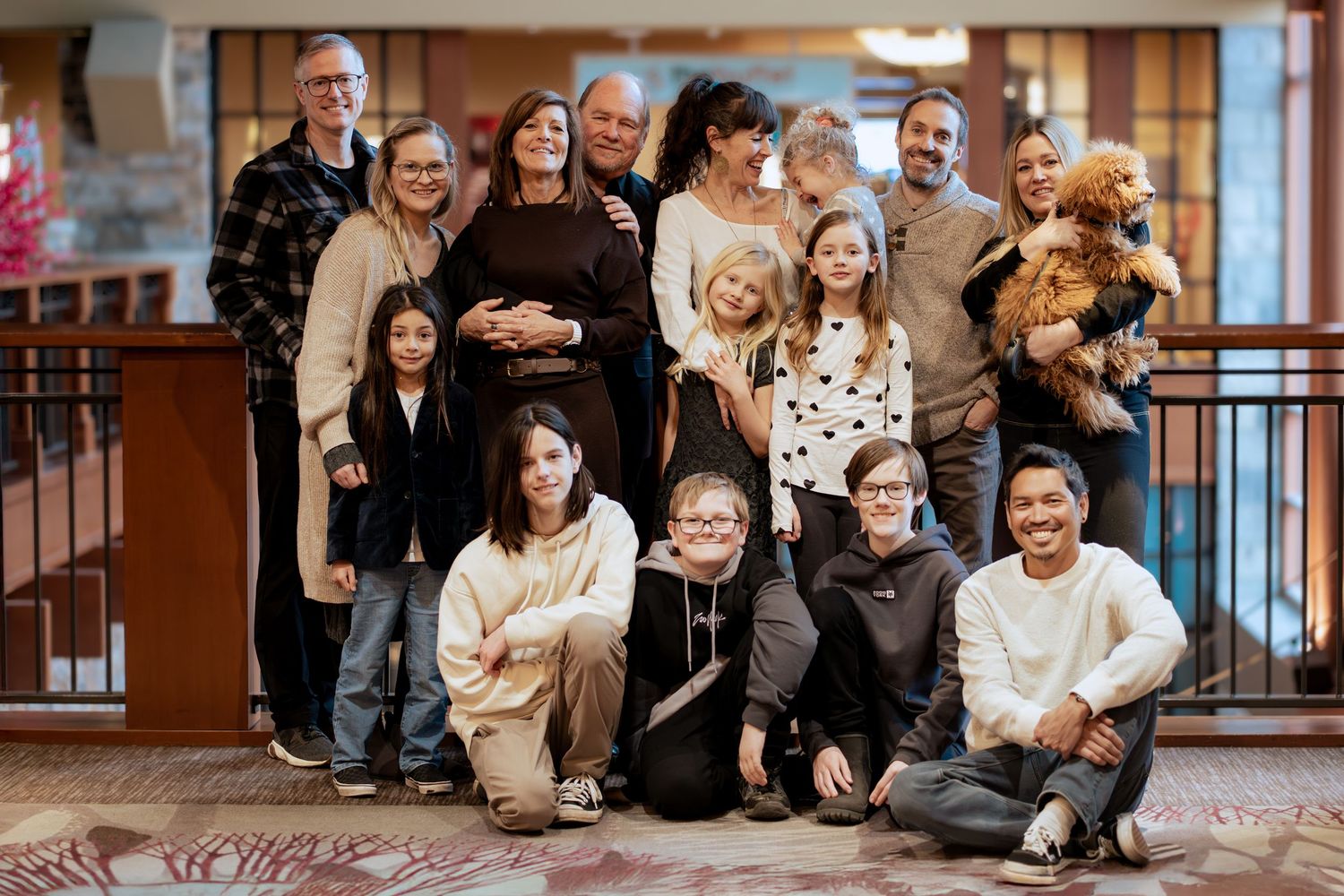 Large multigenerational family group posing together indoors, smiling for a portrait in a warmly lit hotel lobby.
