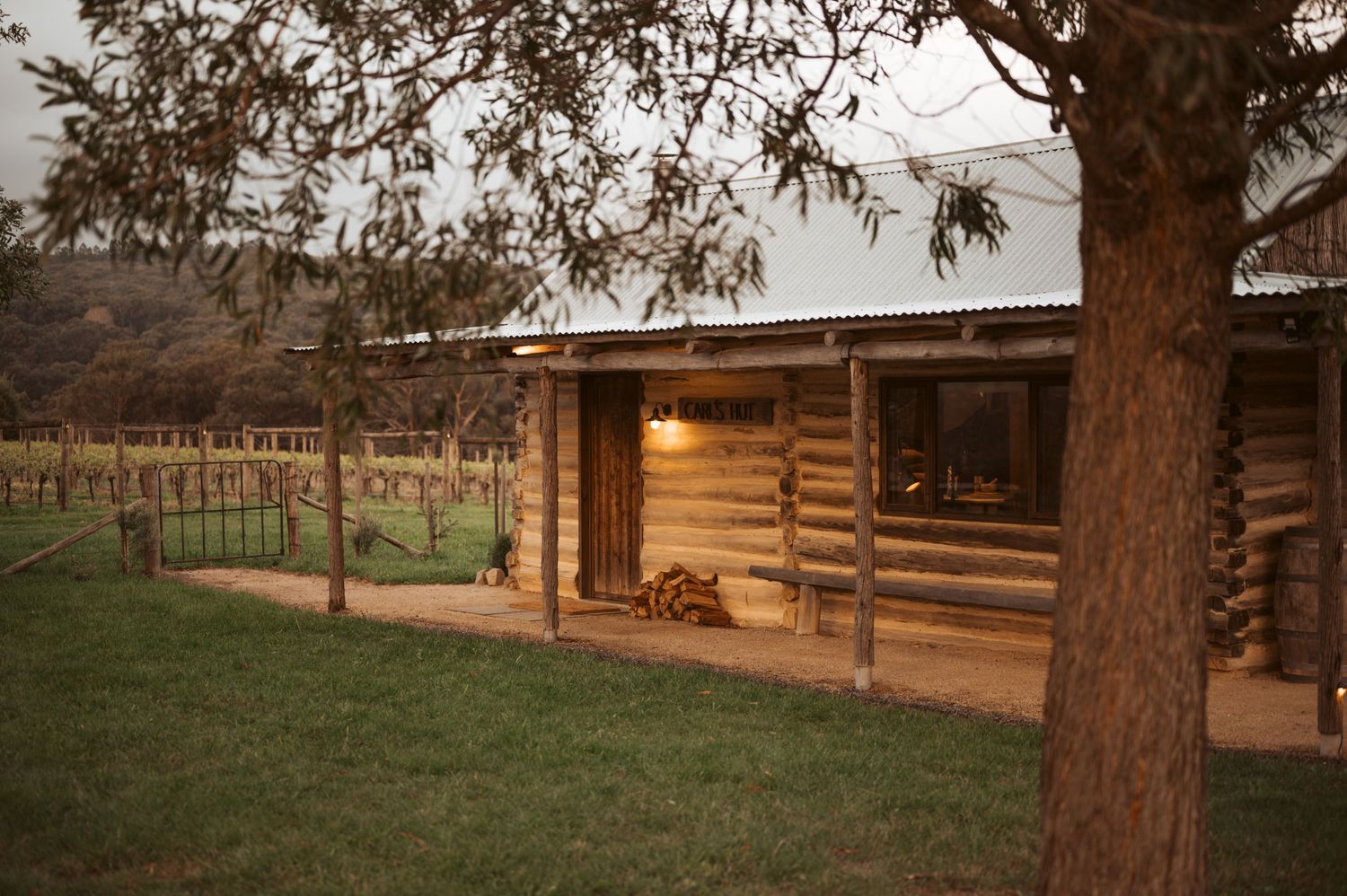 Charming log cabin with timber porch overlooking vineyard, nestled among eucalyptus trees in Australian countryside.