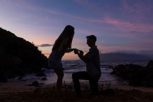 Silhouette of romantic couple during beach proposal at twilight with colorful sky backdrop.