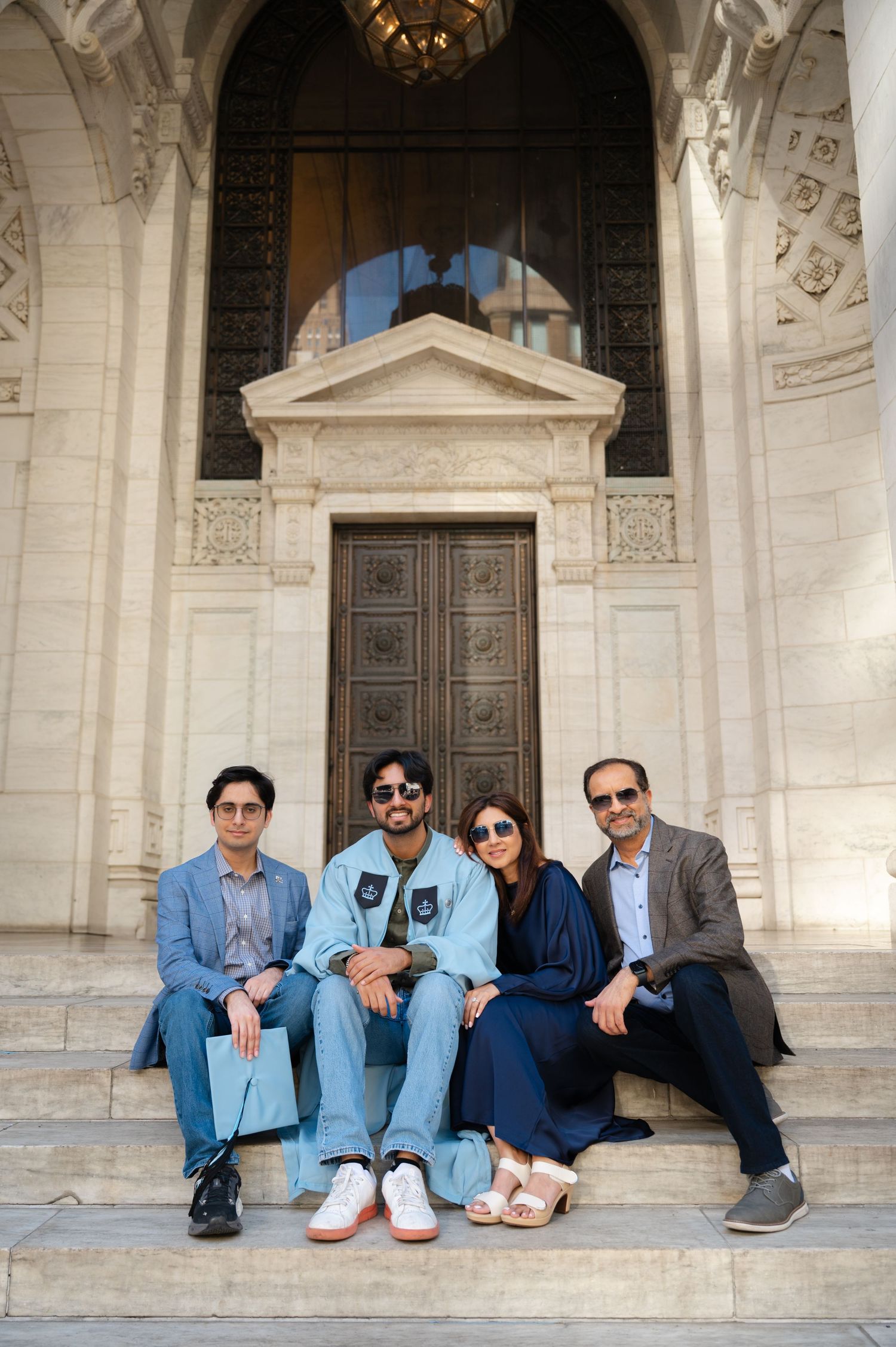 Four people sitting on marble steps in front of an ornate building with large wooden doors.