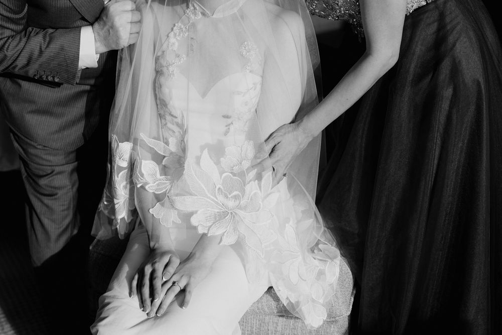 Black and white photo of a bride in a lace wedding dress with veil, surrounded by wedding guests.