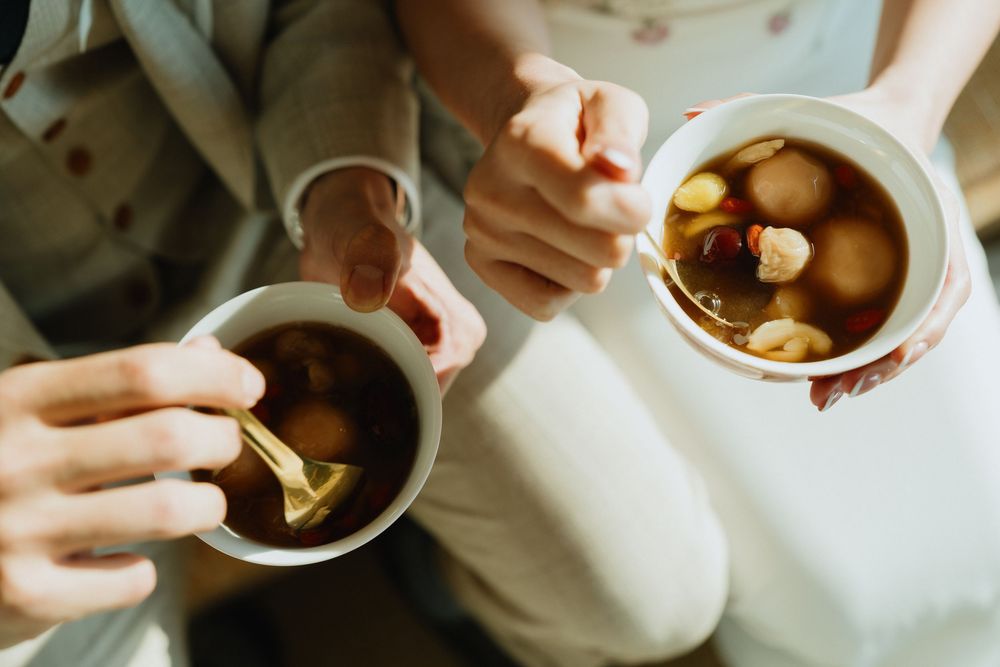 Two people holding mugs of hot tea with fruit, sharing a warm drink together at a cozy gathering.