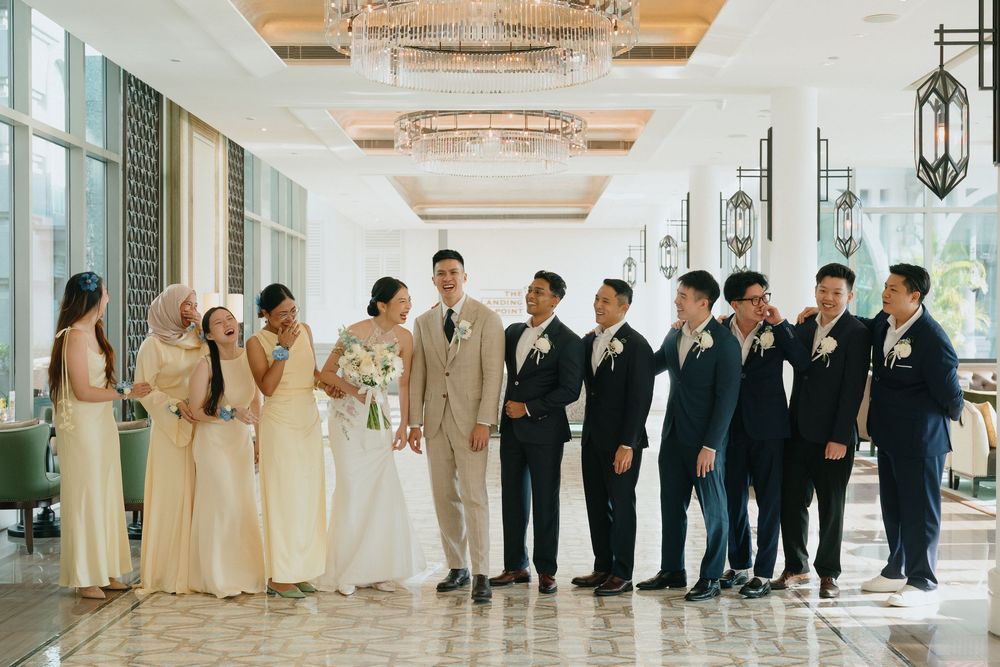 Wedding party poses in elegant venue with bridesmaids in cream gowns and groomsmen in navy suits beside bride and groom.