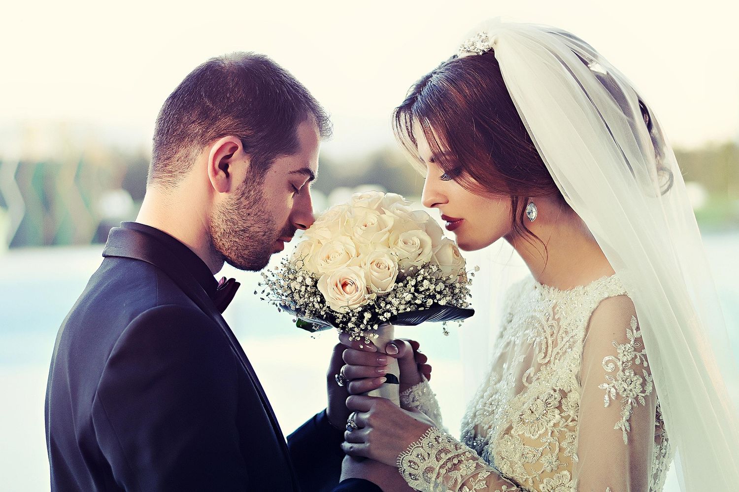 Bride and groom sharing an intimate moment over a white rose bouquet on their wedding day.