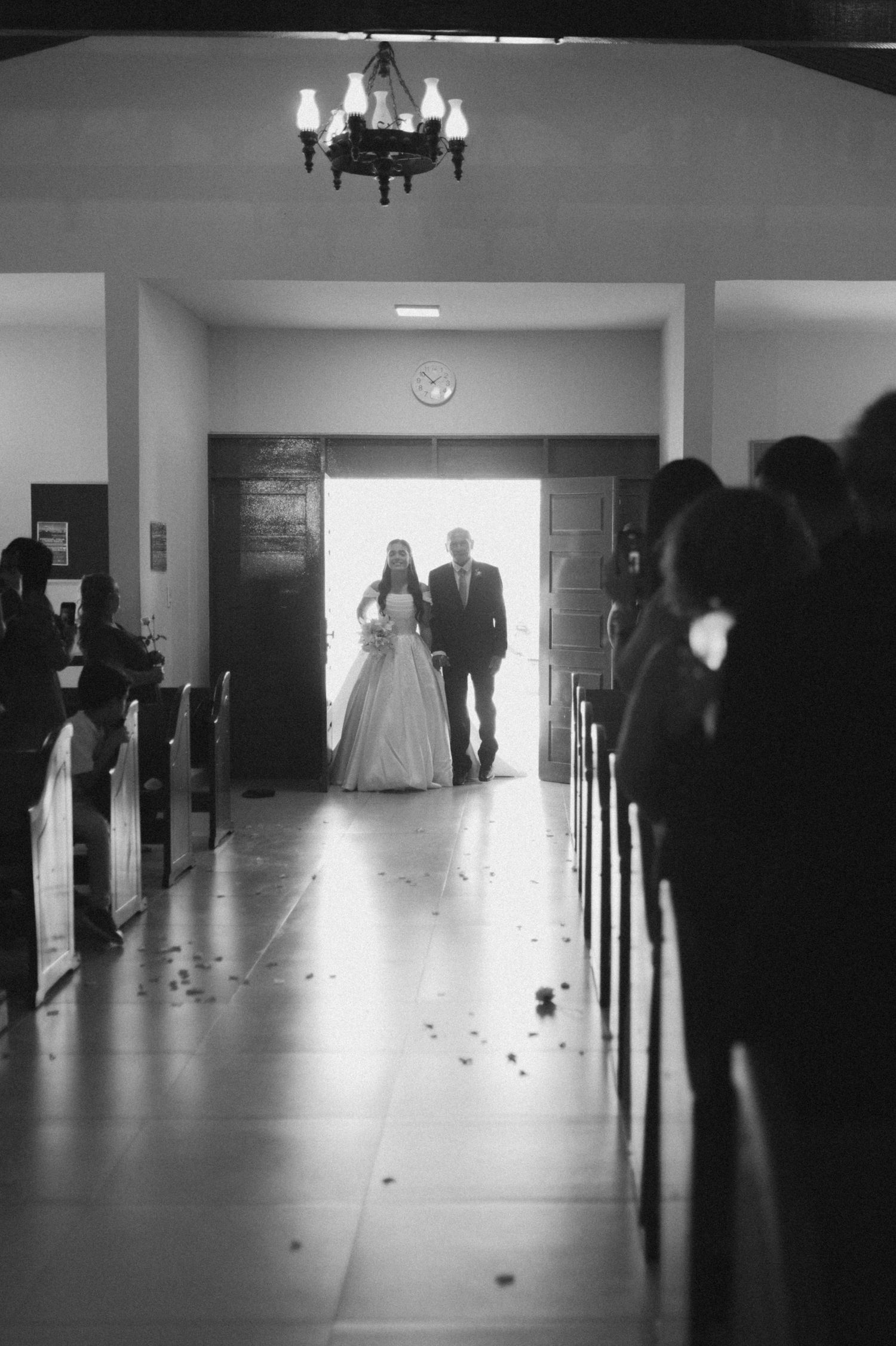 Black and white photo of a bride walking down the church aisle with her escort at a wedding ceremony.