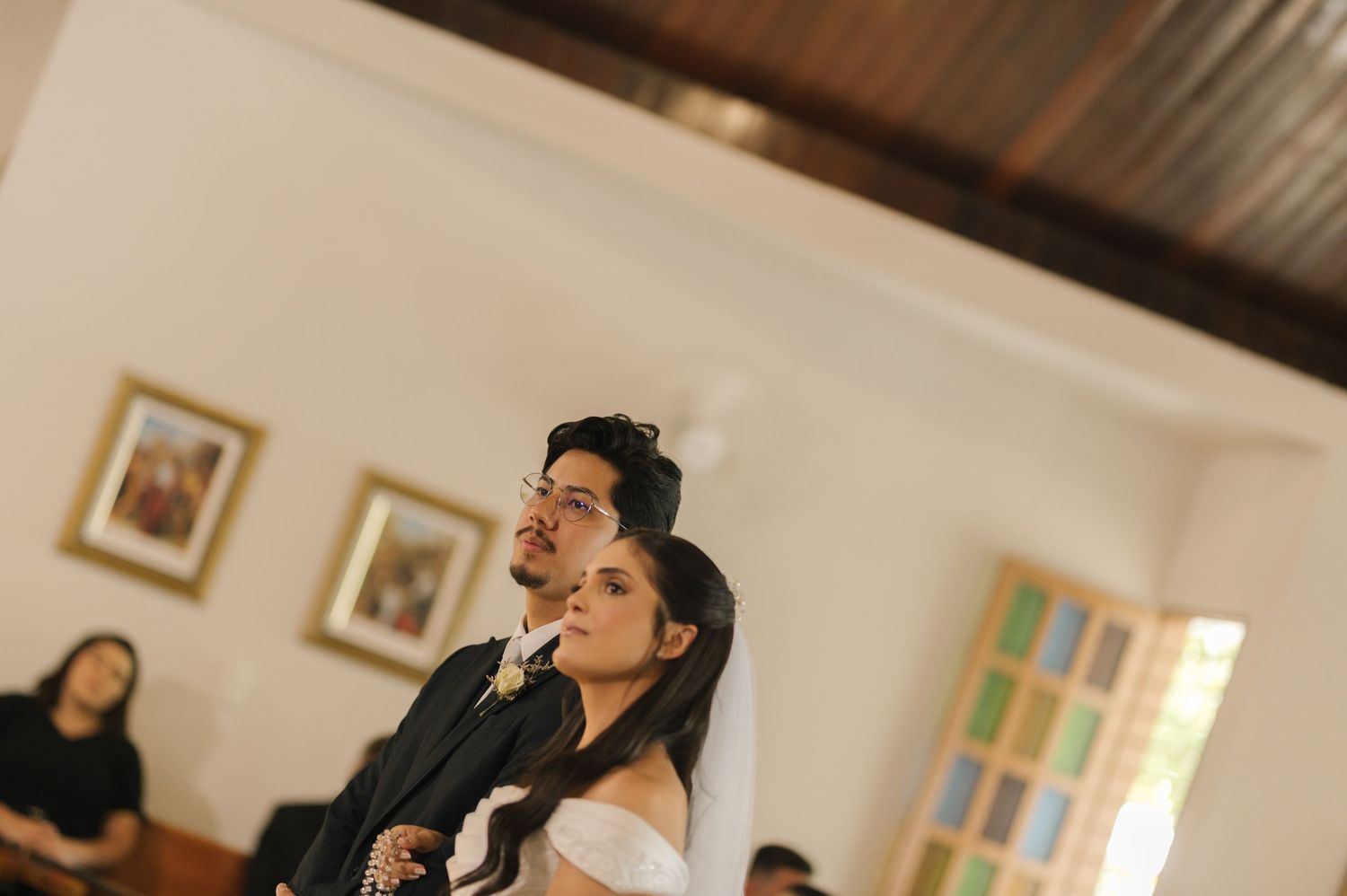 Bride and groom stand together during wedding ceremony inside a church with wooden ceiling.