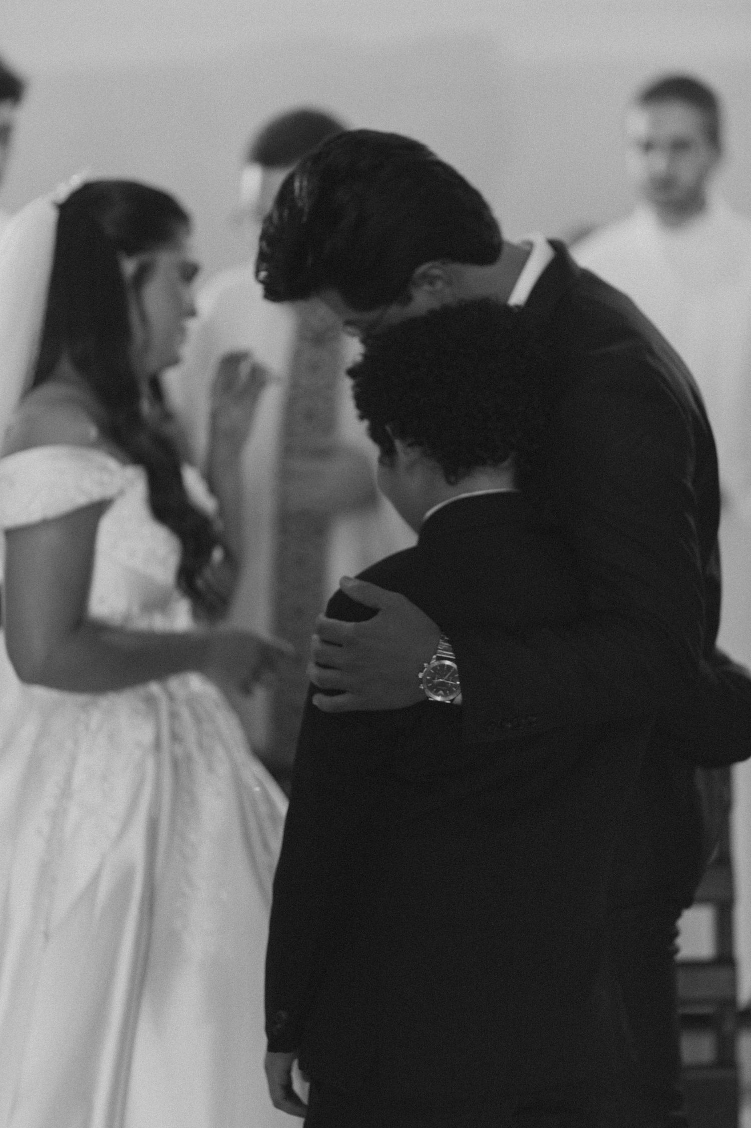 Groom embraces a young boy in black and white wedding ceremony photo.
