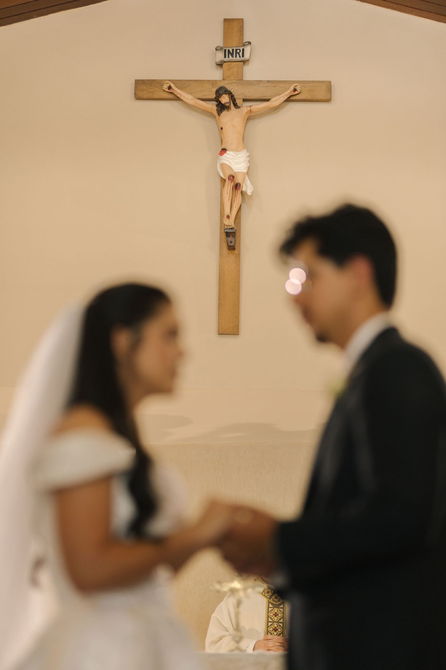 Catholic wedding ceremony with bride and groom holding hands beneath a crucifix in a church.