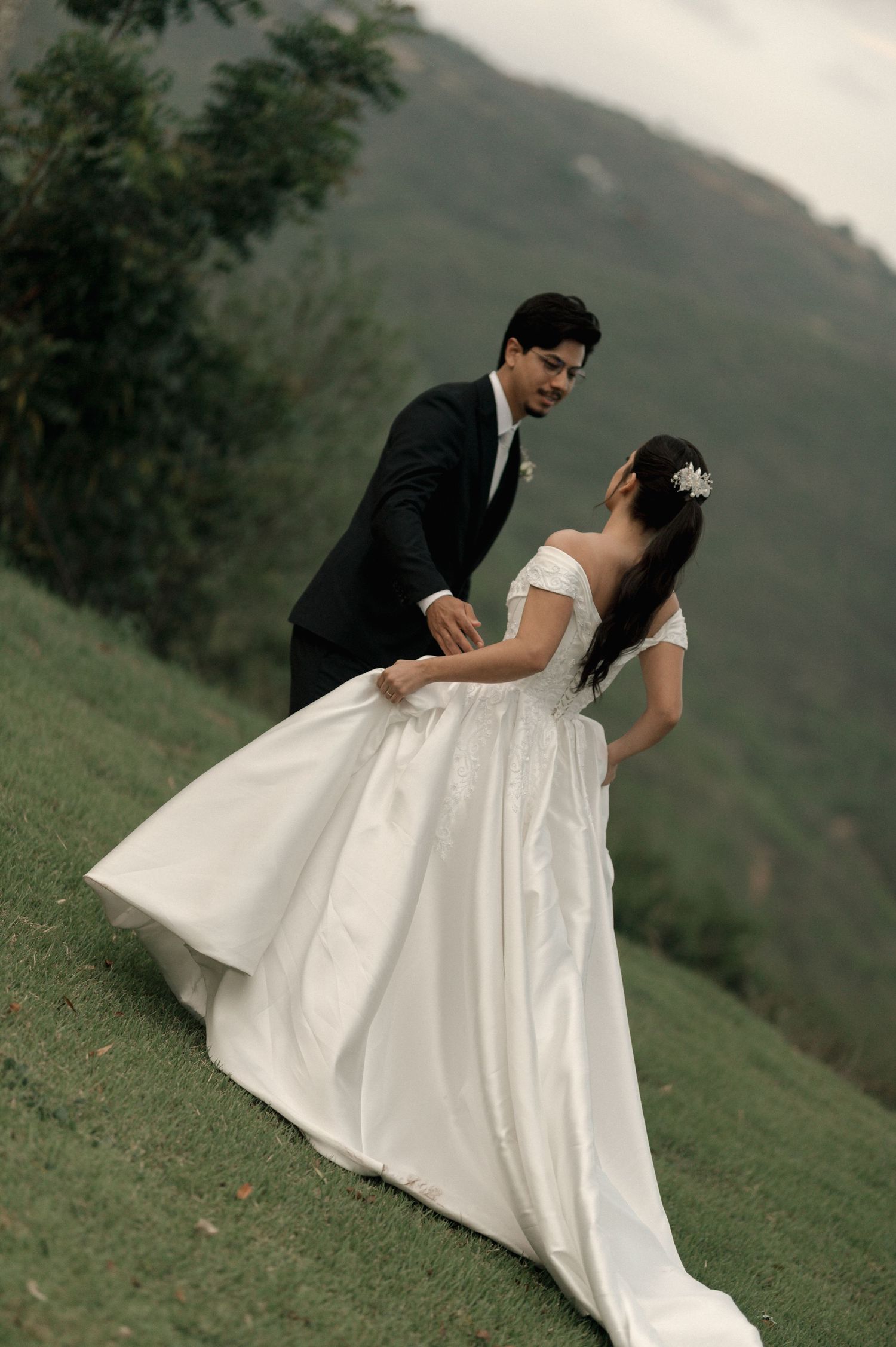 A bride and groom share a romantic dance on a lush green hillside with misty mountains in the background.