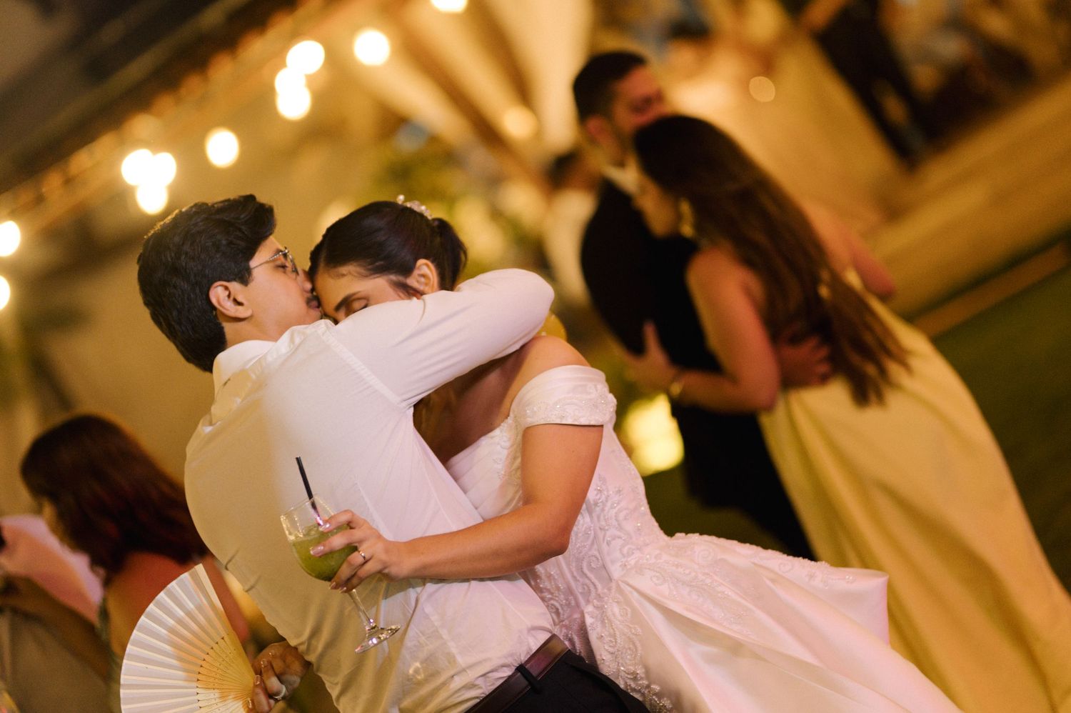 Two children share a warm hug while dancing at a wedding reception with string lights in the background.