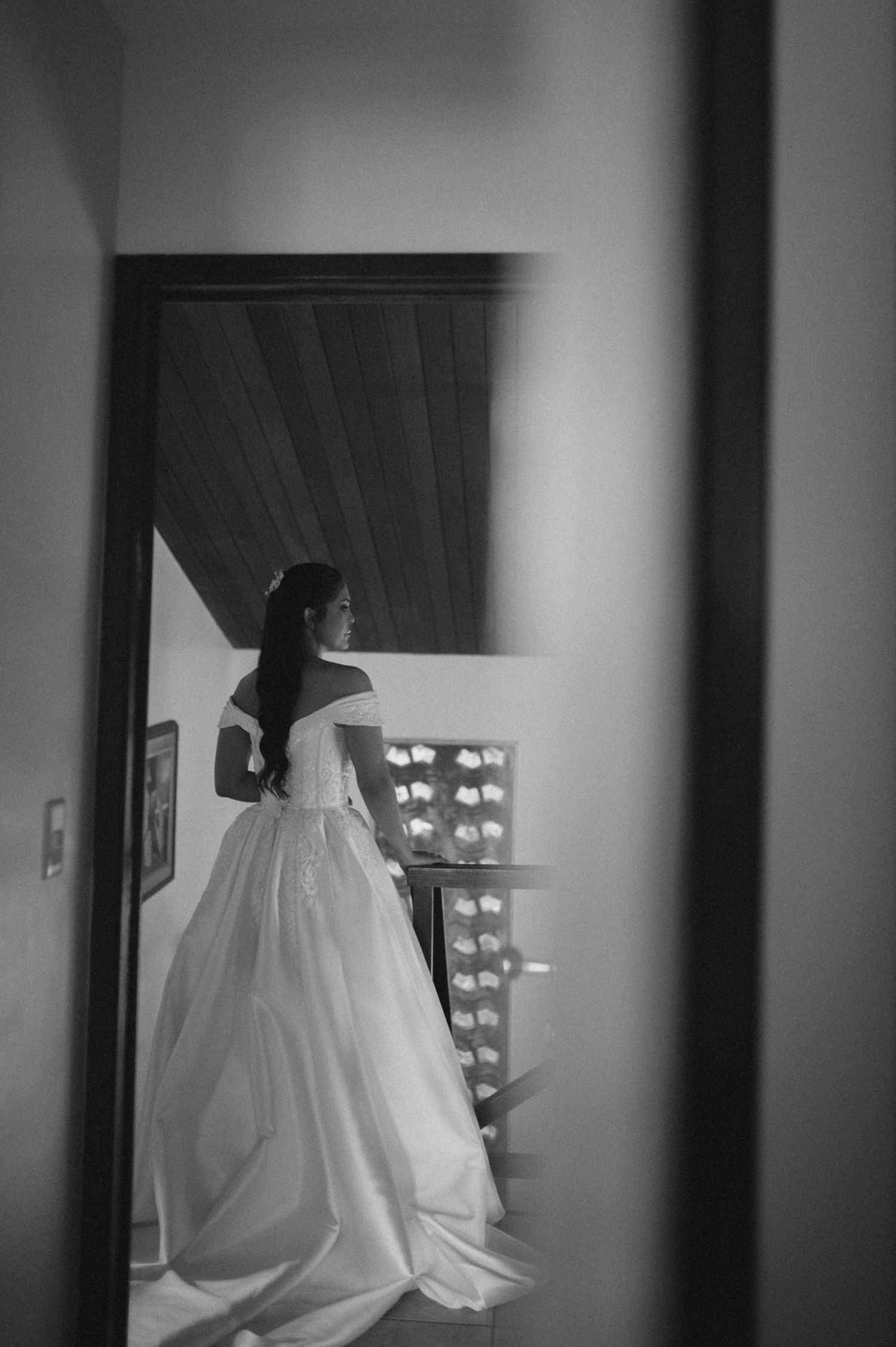 Black and white photo of a bride in a elegant ball gown wedding dress standing in a doorway with vanity lights.
