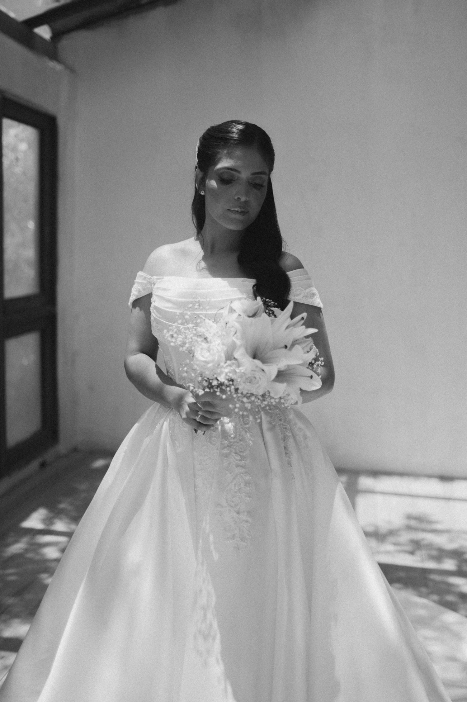 Bride in off-shoulder ball gown holding floral bouquet, black and white wedding portrait.