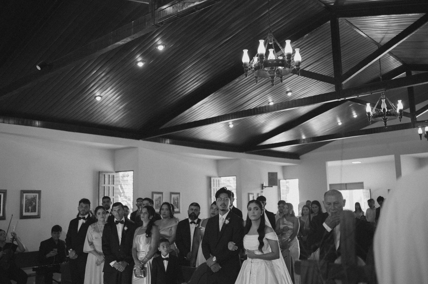 Black and white photo of a wedding ceremony with bride and groom at the altar surrounded by guests in an elegant venue.