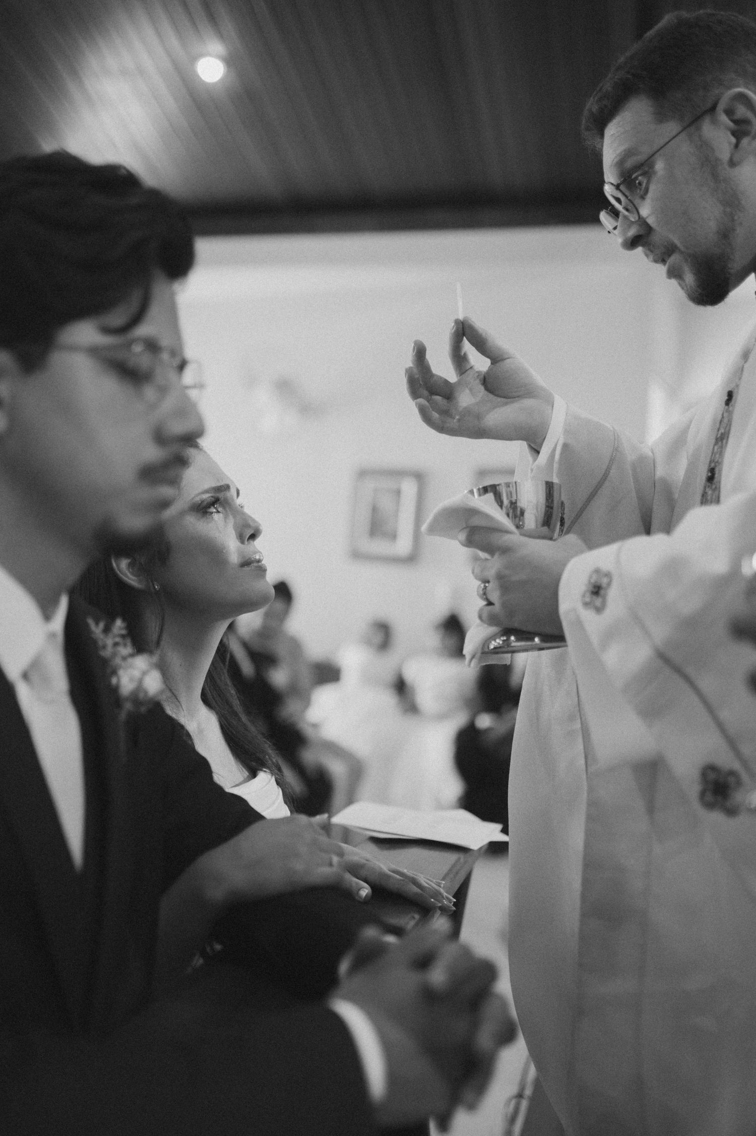 Black and white close-up of a priest blessing a couple during a wedding ceremony in a church.