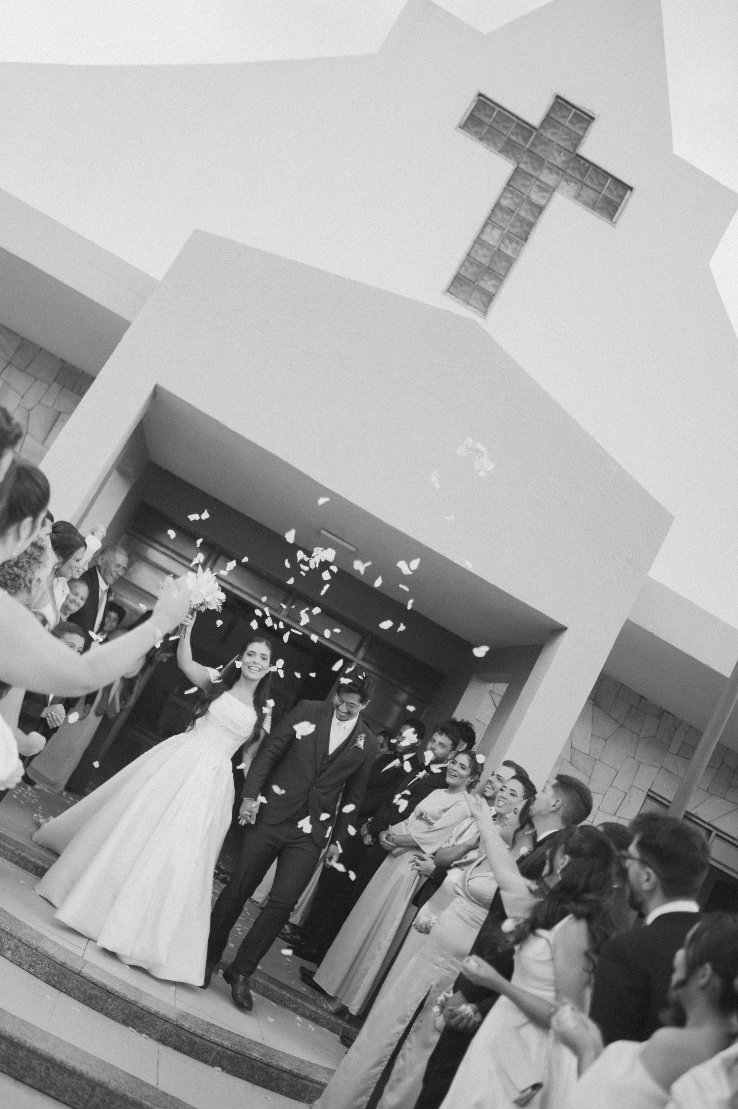 Black and white photo of a joyful bride and groom exiting a church as guests throw confetti at their wedding.