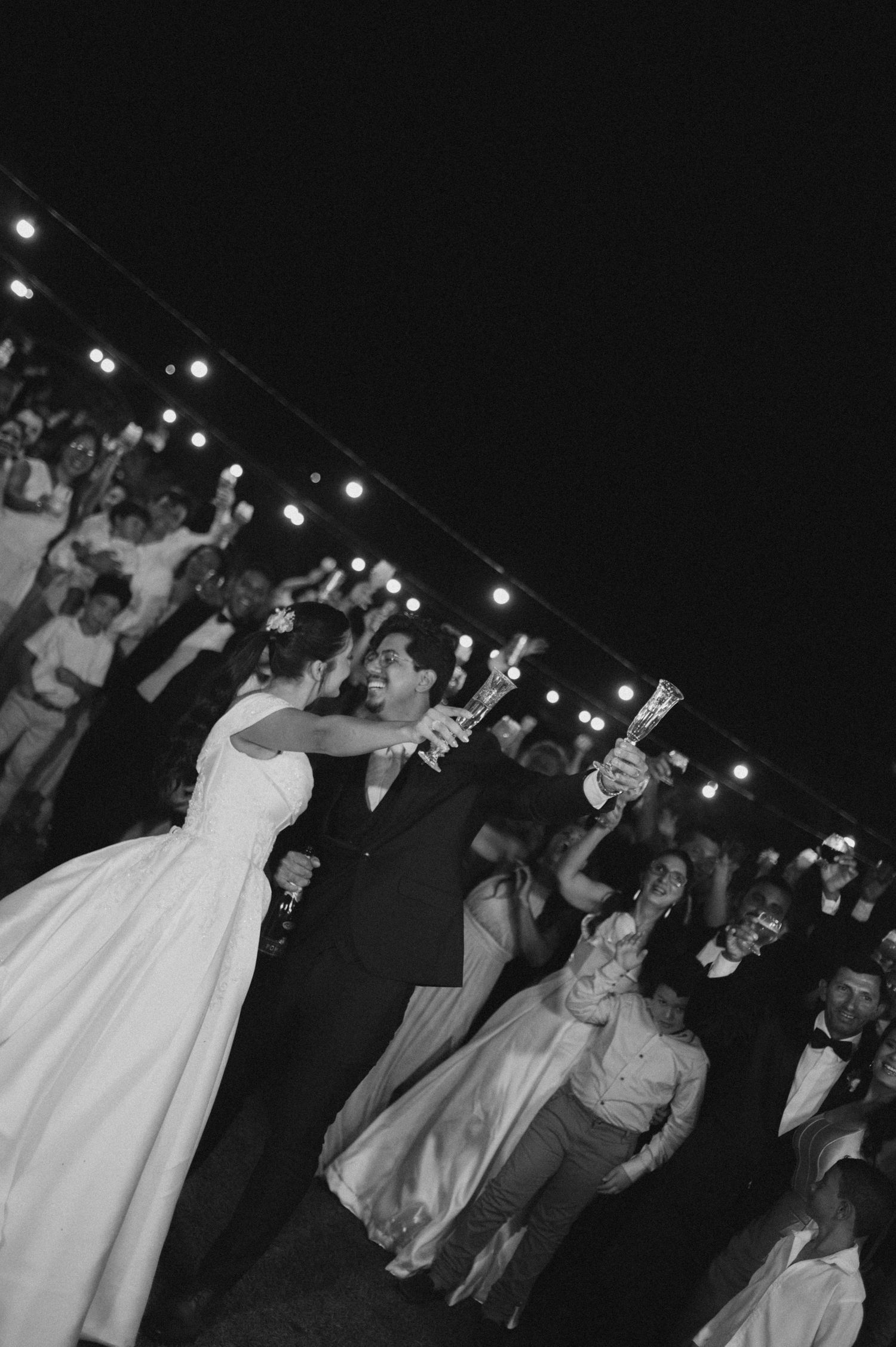 Black and white wedding photo of bride and groom sharing first dance surrounded by guests holding lights.