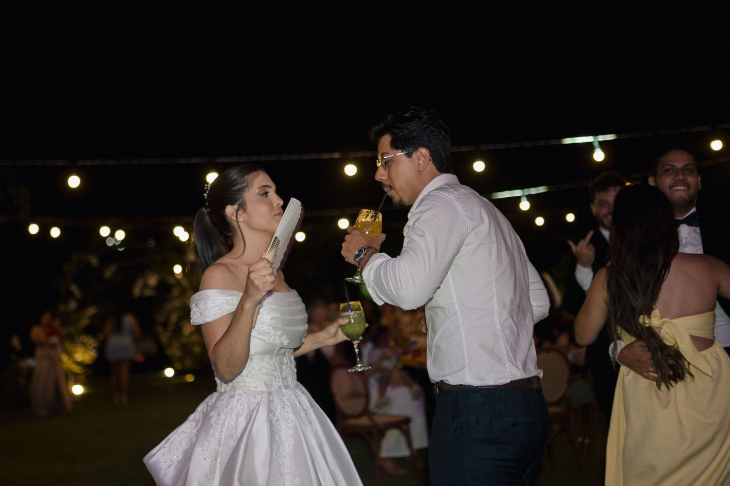 Bride and groom sharing a romantic dance outdoors at night, holding champagne glasses at their wedding reception.