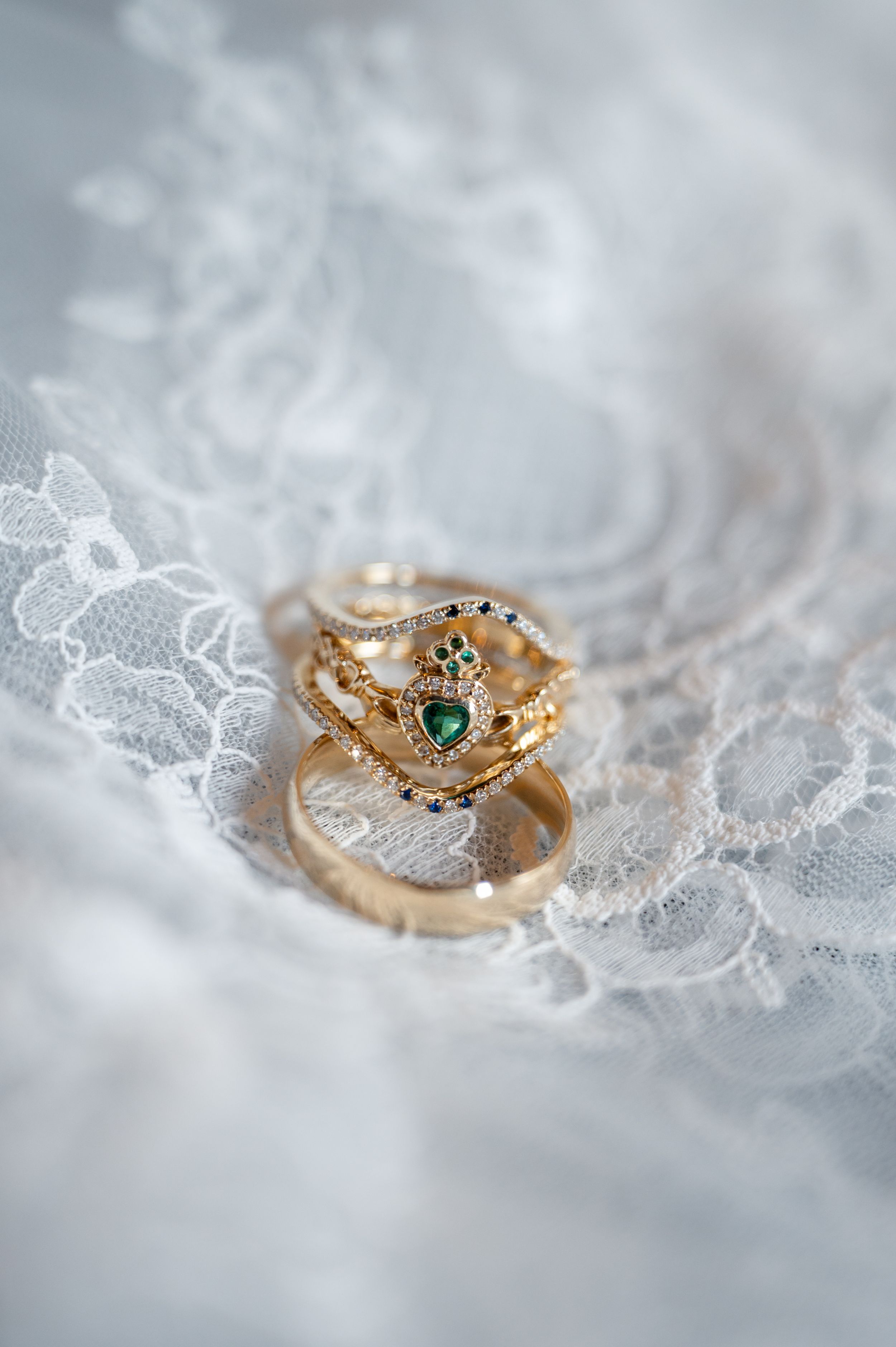 Gold rings with emerald gemstone displayed on white lace fabric, perfect for wedding jewelry inspiration.