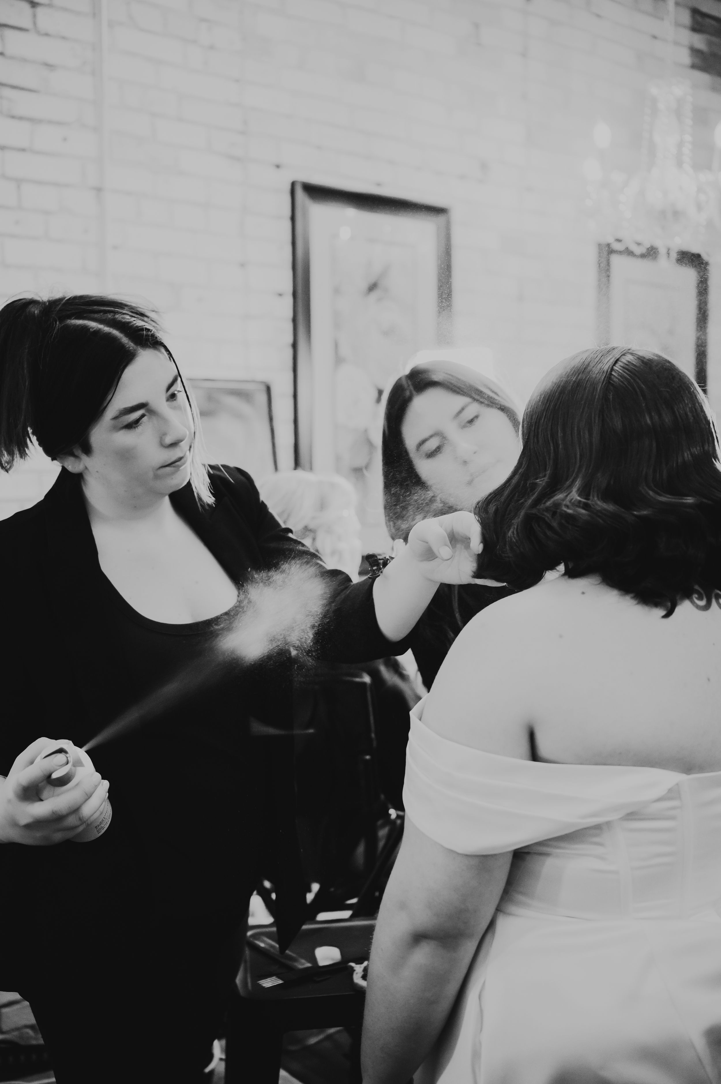 Makeup artist applying setting spray to a bride in a white gown during wedding preparations in black and white.