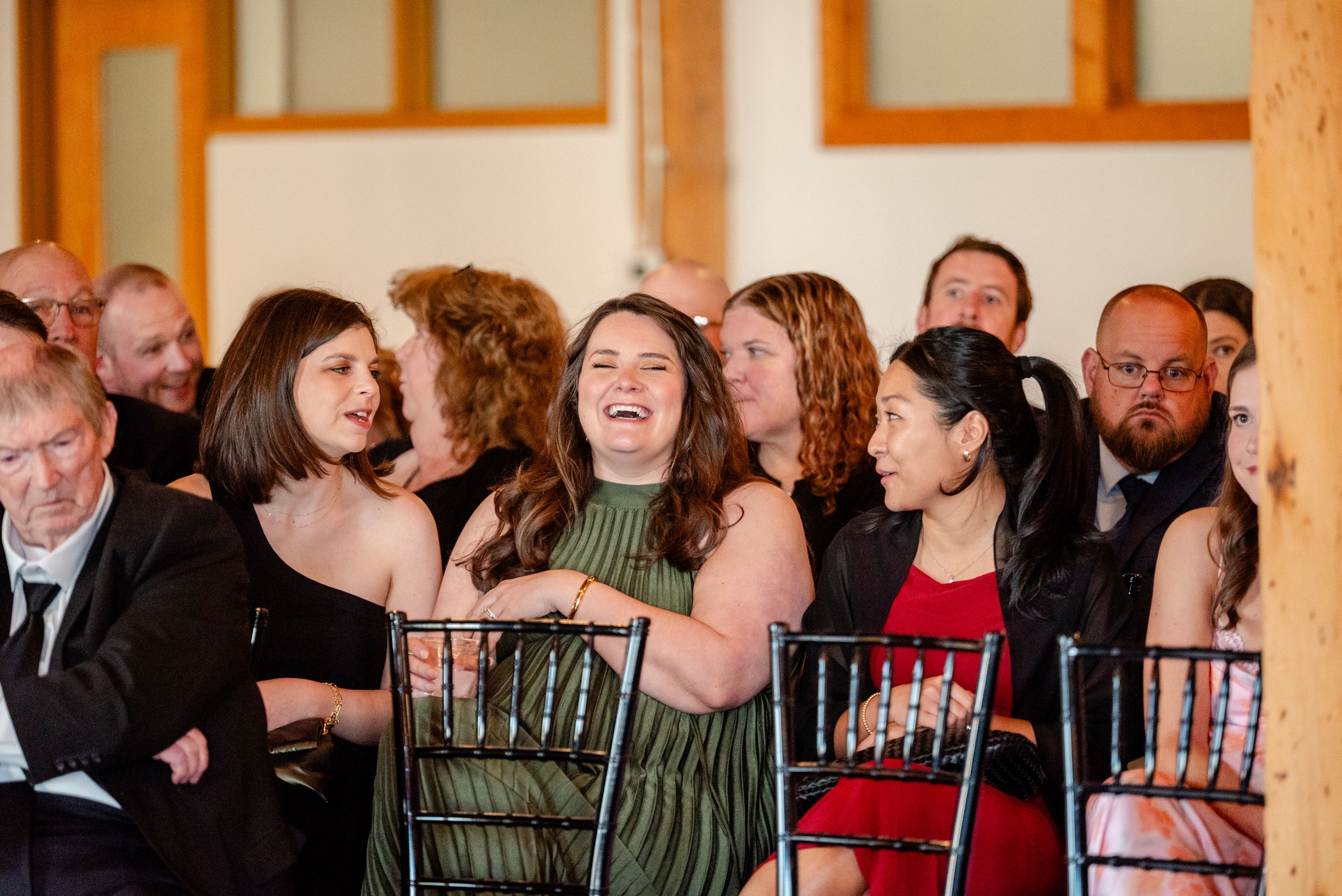 Wedding guests laughing and smiling joyfully while seated at an indoor ceremony.
