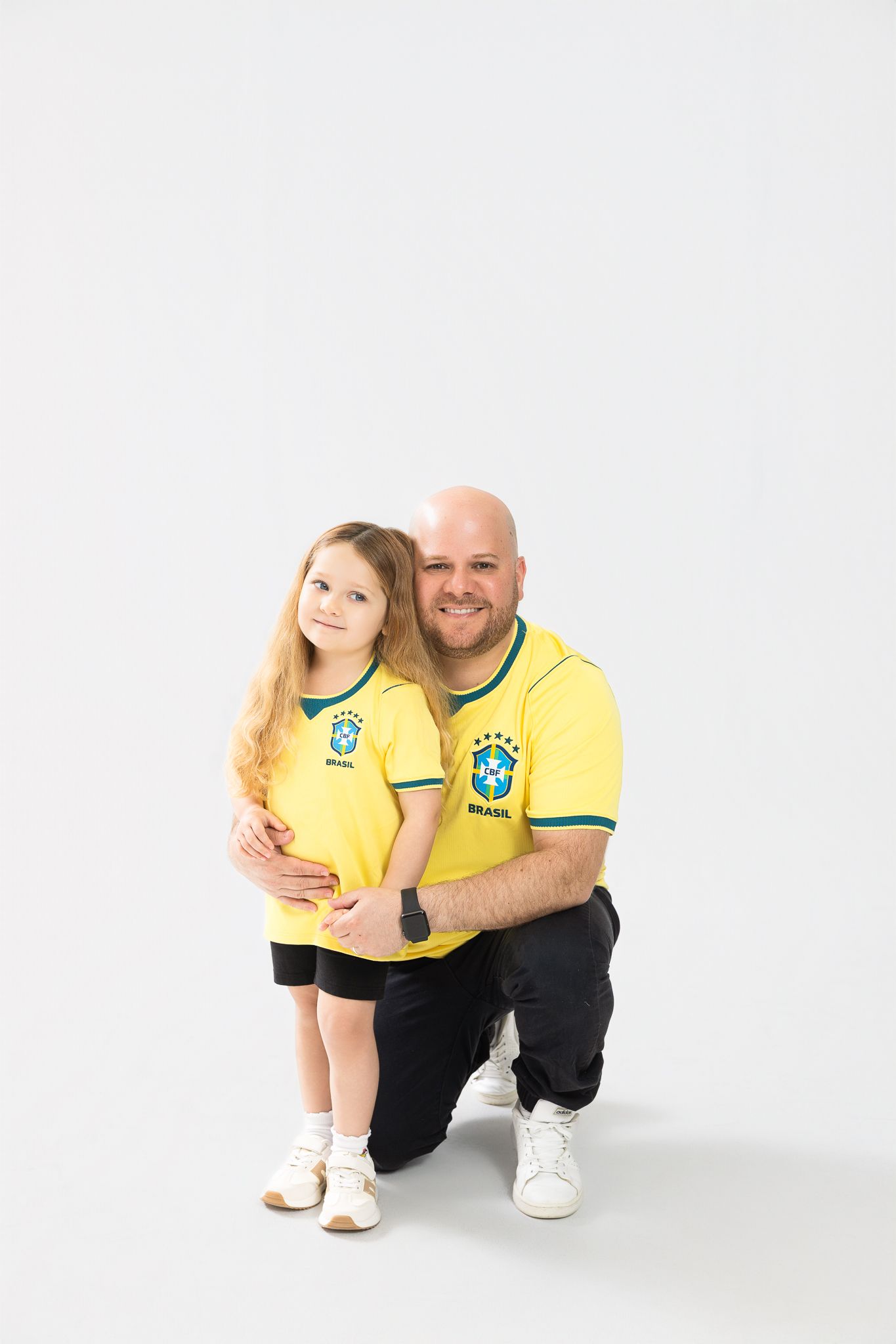 Father and daughter wearing matching yellow Brazil soccer jerseys posing together on white background.