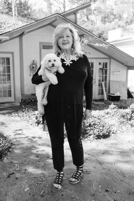Smiling woman holding a white fluffy dog outside a cottage home.