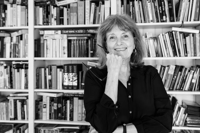 Woman smiling in front of a large bookshelf filled with books.
